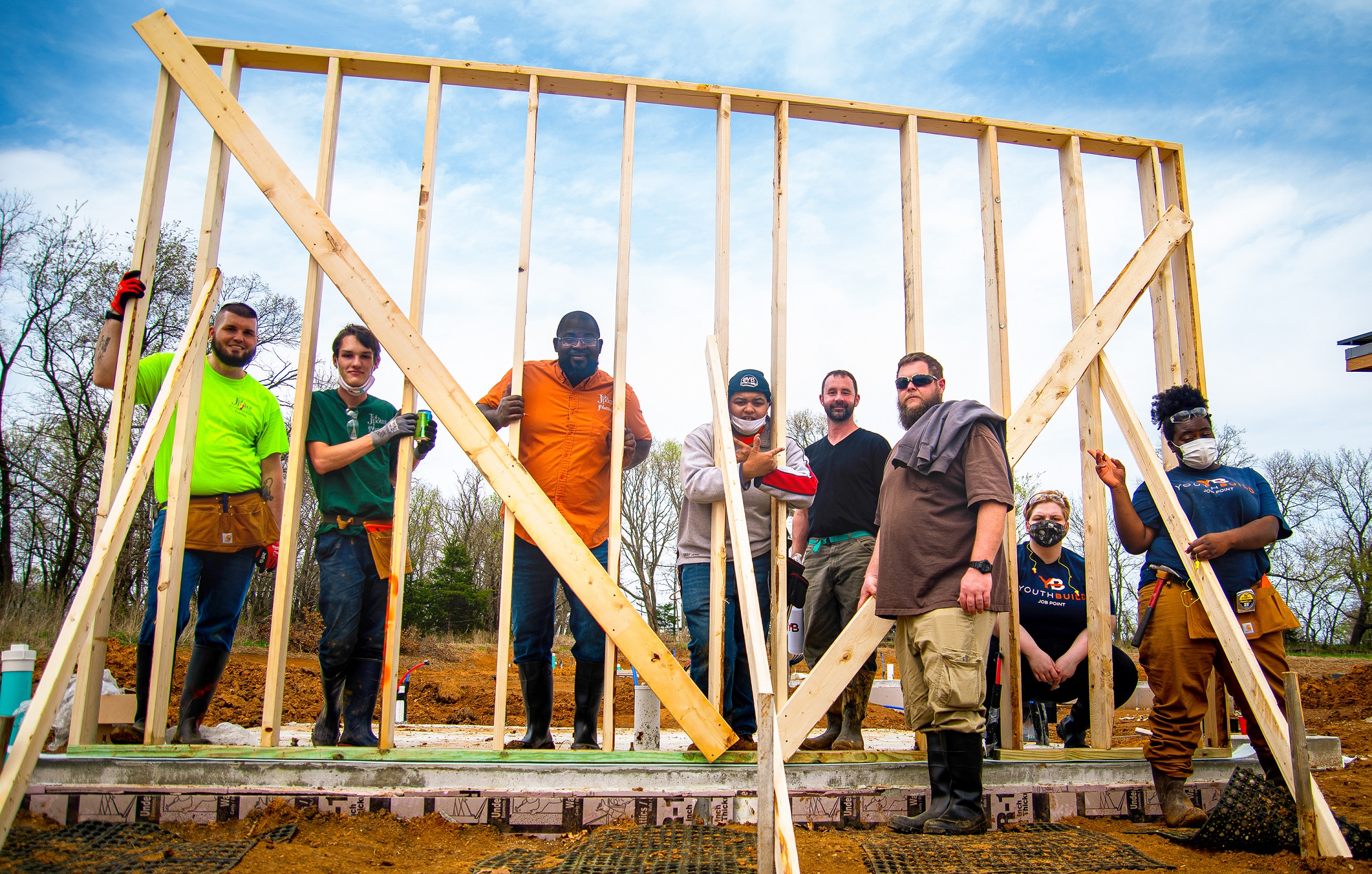 People stand in the midst of a framed wall on a new construction site.