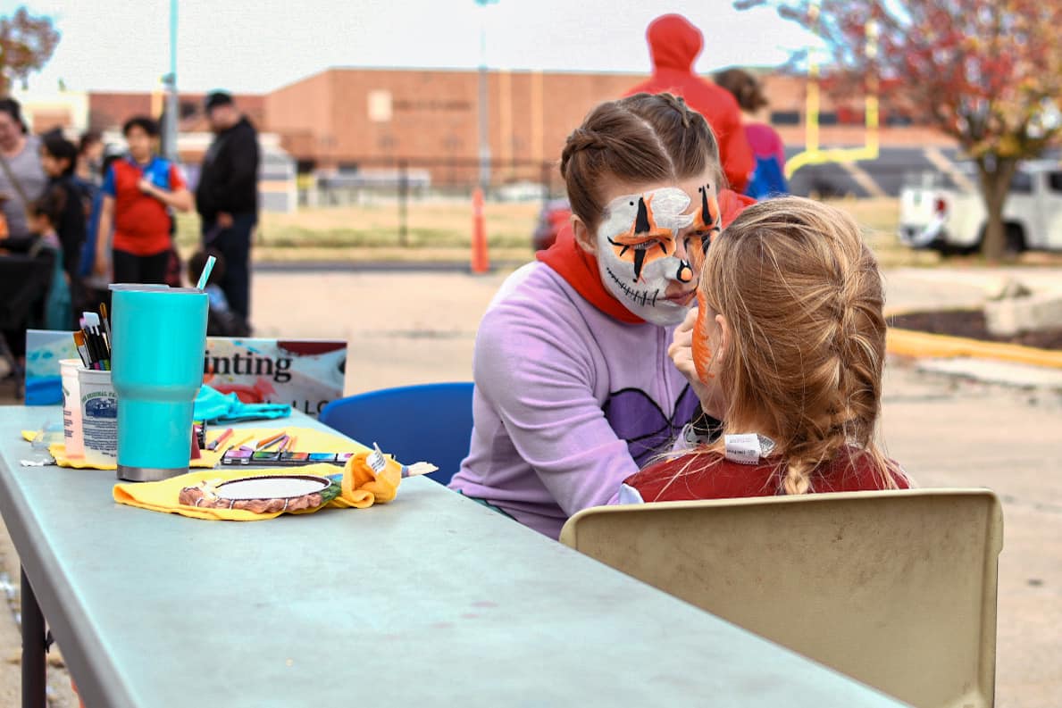 Face painter decorates a kids face while they attend the halloween block party