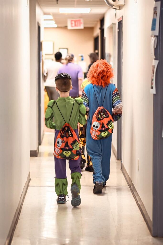 children in costume walk down a hall.