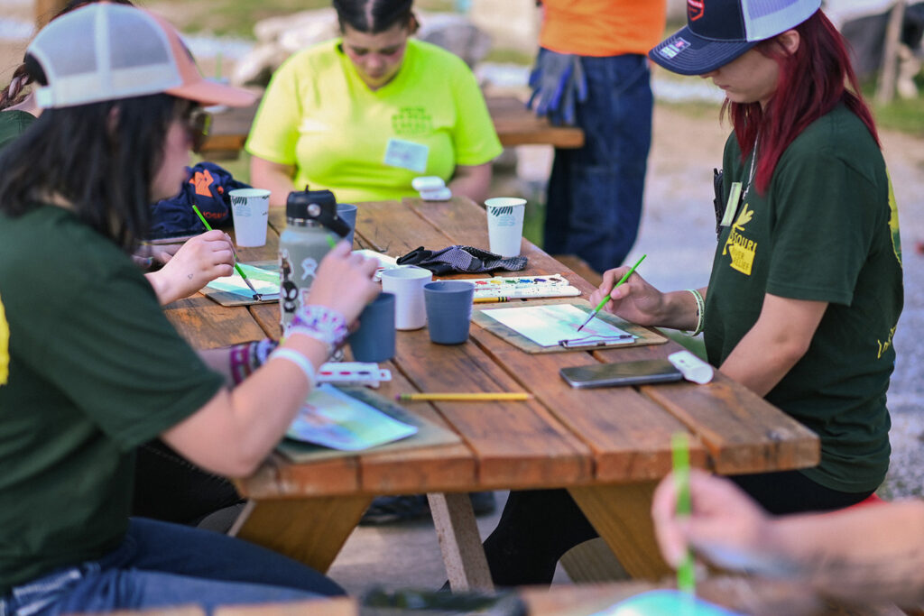 Young people sitting at a table water color painting. 