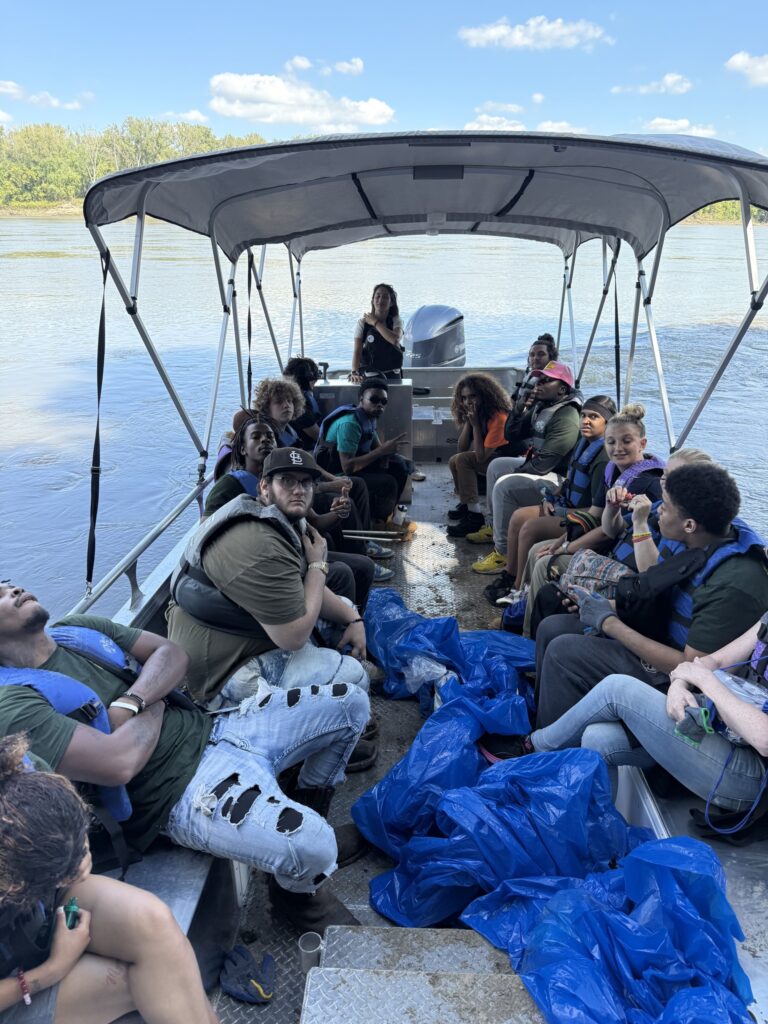 Young people sit on a boat with garbage bags at their feet.