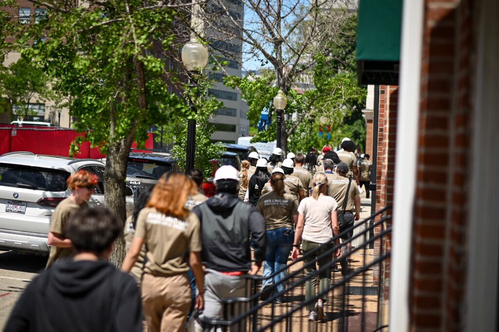 A large group of students from YouthBuild programs across the state walk down the sidewalk toward the Missouri State Capitol in the distance.