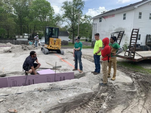 Instructor stands with students showing them how plumbing will be installed in the foundation of a new home.